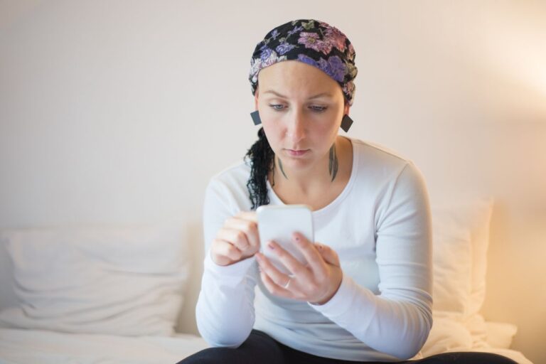Woman using smartphone from bed during recovery — keeping doctor updated via telemedicine after surgery abroad