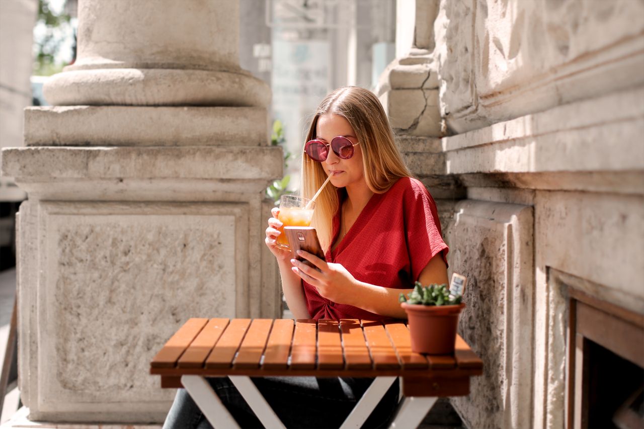 Traveler using phone at an outdoor cafe — hotel WiFi does not reach the restaurant down the street