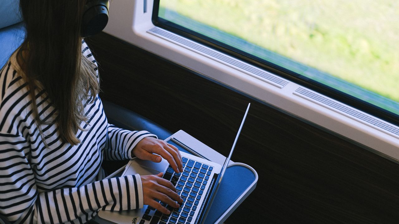 Passenger using a laptop on a European train, where train WiFi speeds average 7.6 Mbps